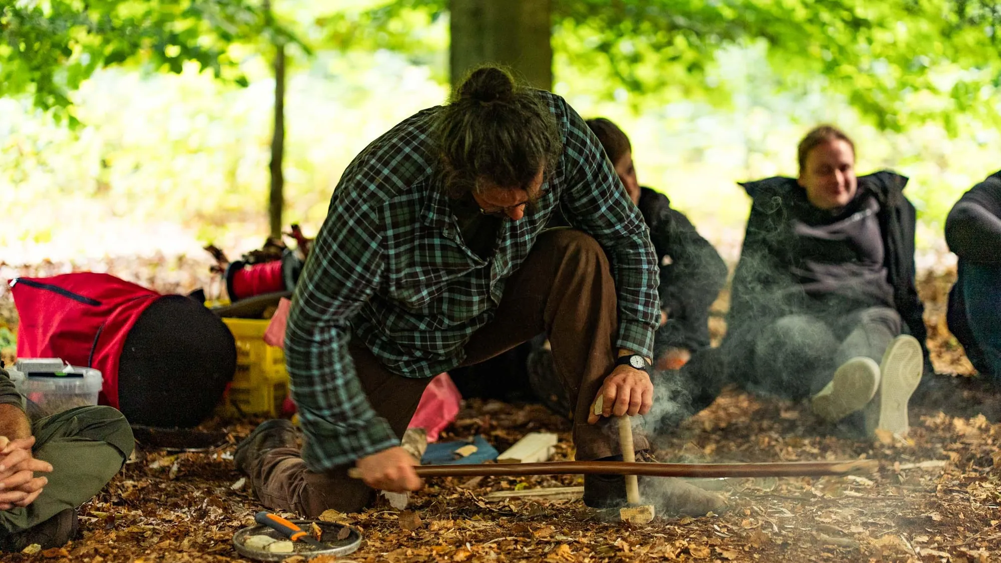 Team am Lagerfeuer im Wald, jemand entzündet Feuer