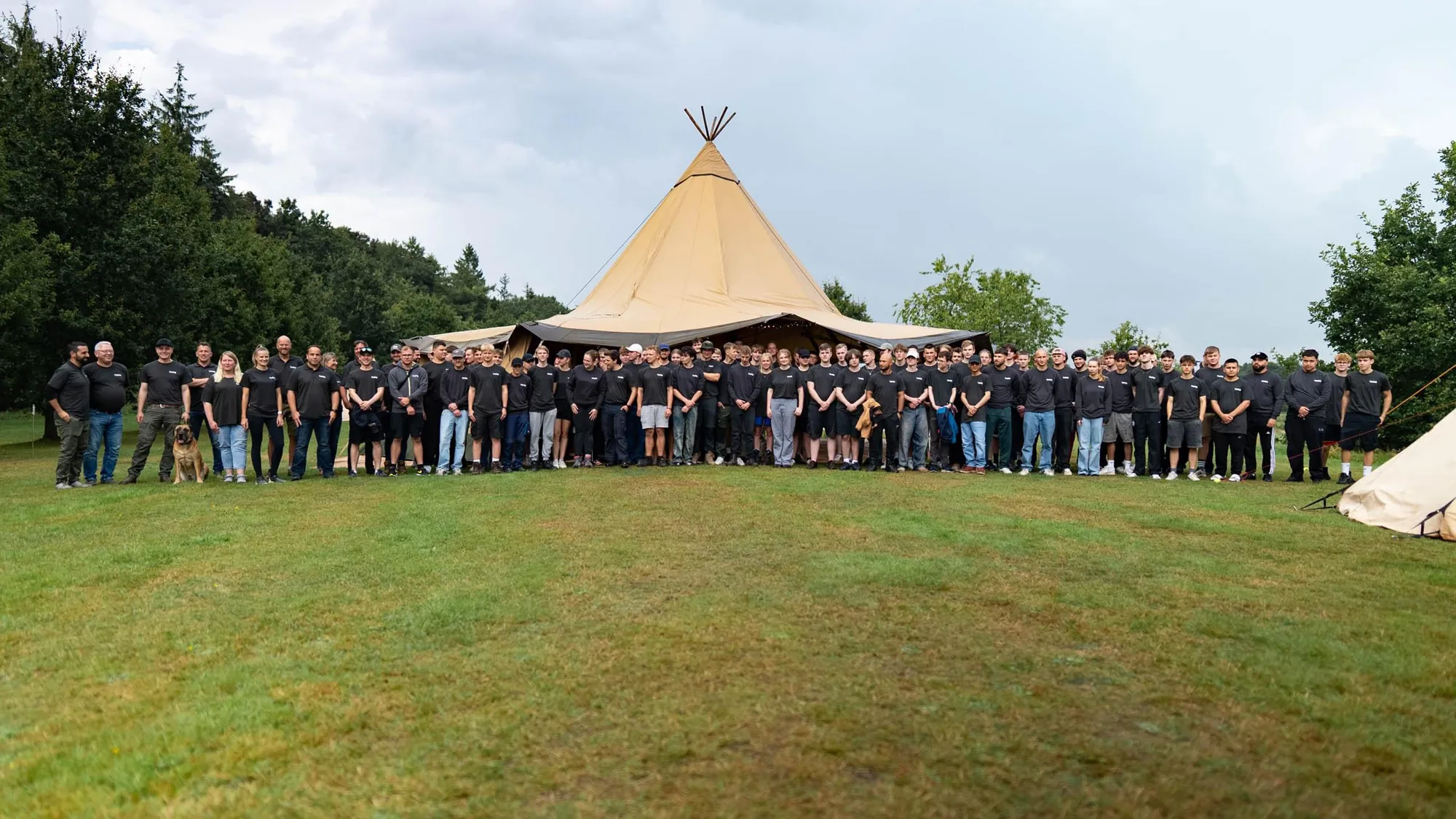 Großes Team vor einem Tipi auf einer Wiese